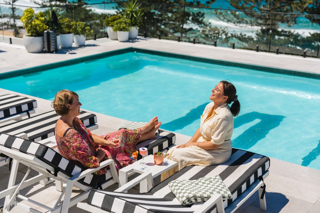 Two people laugh and enjoy drinks at Manly Pacific's rooftop pool